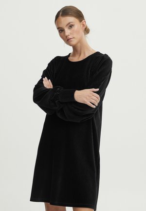 Musta corduroy-mekko, jossa on pitkät puff-hihat, pyöreä pääntie ja rento malli. Ominaisuuksiin kuuluu pystysuora ribbitekstuuri ja polvimittainen helma.