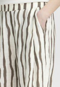 Lightweight, cream pants with brown vertical stripes; features a side pocket and a relaxed fit showing soft, textured fabric.