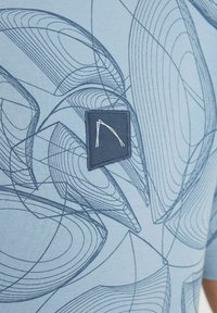 Šviesiai mėlynas marškinis, puošiamas sudėtingais tamsiai mėlynais linijiniais raštais. Į komplektą įeina tamsiai mėlyna audinio etikete su balta logotipu. 3/4 ilgio rankovės.