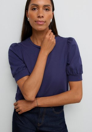 Haut bleu marine à manches courtes bouffantes, encolure ronde, texture lisse, porté avec un jean taille haute. Design minimaliste, sans motifs.