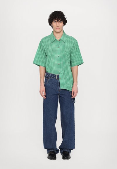 Green checked short-sleeve shirt with buttons, paired with wide-leg blue jeans. Black shoes complete the outfit.
