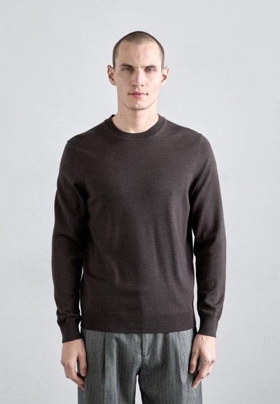 Brun strikket sweater med rund hals og lange ærmer, parret med grå, lodret stribede bukser med høj talje.