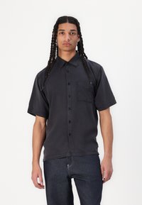 Schwarzes kurzärmliges Hemd mit Knöpfen aus leichtem Baumwollstoff, mit einer Brusttasche, klassischem Kragen und entspannter Passform.