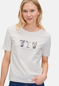 T-shirt à manches courtes gris clair avec des graphiques de cocktails et le texte "cocktails d'abord" en doré rose métallique. Tissu doux et lisse.