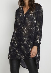 Camicia lunga nera a fantasia in tessuto leggero con scollatura a V, maniche lunghe e spacchi laterali, caratterizzata da schizzi astratti crema e verdi.