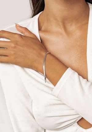 Silver-tone metal bracelet, sleek snake chain design with a smooth texture, worn on a wrist, paired with a white ribbed top.