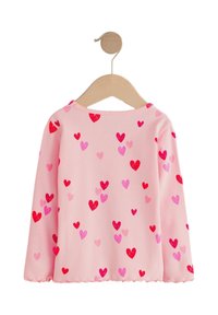 Lyserød langærmet skjorte med ribt tekstur, dekoreret med spredte røde og lyserøde hjerteprints. Rund halsudskæring og bølget kantdetalje.