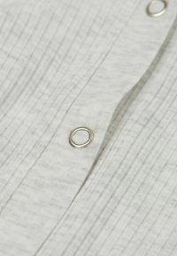 Bílá strukturovaná látka s vertikálními pruhy, obsahující kovový knoflík a dírku na knoflík. Detailní záběr, který zvýrazňuje texturu látky.