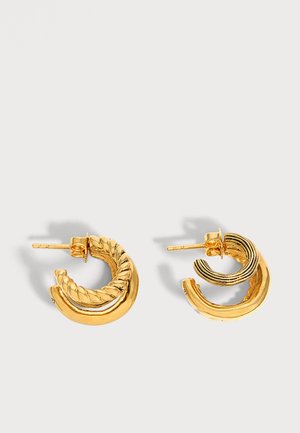 Paire de petites boucles d'oreilles créoles en or avec des sections torsadées et lisses sur un fond clair uni.