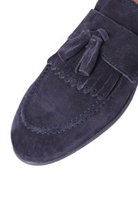 Mocassino in suede navy con dettagli in frange, cuciture a contrasto e punta arrotondata. Presenta nappe sulla parte superiore e una suola piatta in gomma.