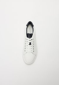 Sneakers din piele albă cu accente negre, vârf rotund, sistem de prindere cu şireturi, şi branding proeminent pe interior. Textură netedă cu detalii minime.