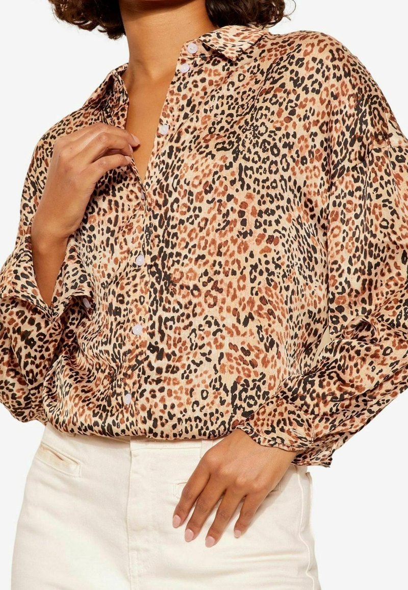 Blusa con stampa leopardata in tessuto leggero, con colletto classico, bottoni e maniche lunghe con dettagli sui polsini. La palette di colori include beige, nero e ruggine.
