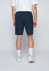 Námořnické modré šortky s texturovaným vzorem, elastickým pasem a bočními kapsami, spárované s bílými ponožkami a světlými teniskami.