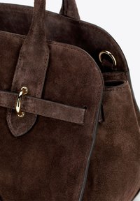 Borsa a tracolla in suede marrone con forma arrotondata, dettagli in metallo dorato e un manico piatto. L'interno presenta una texture morbida e cuciture pulite.