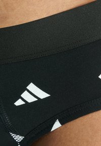 Mustat urheiluhousut valkoisella Adidas-logolla, sileä pinta, tiukka muotoilu ja kontrastiväriset geometriset kuviot alaosassa.