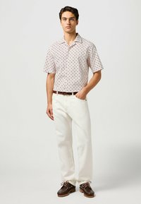 Camisa de manga corta, con un estampado en rosa claro y diseños geométricos. Combinada con pantalones blanco roto y zapatos marrón oscuro con cordones.