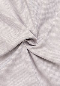 Lichtgrijze stof met een gestructureerd, diamanten patroon en een lichte glans, gedrapeerd en gedraaid om de gladde oppervlakte en diepte te onthullen.