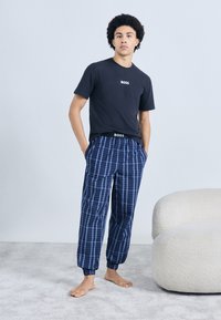 Tricou bleumarin cu logo-ul "BOSS" și pantaloni de pijama în carouri, cu dungi bleumarin și albastre. Croială confortabilă, cu talie și tivuri elastice.