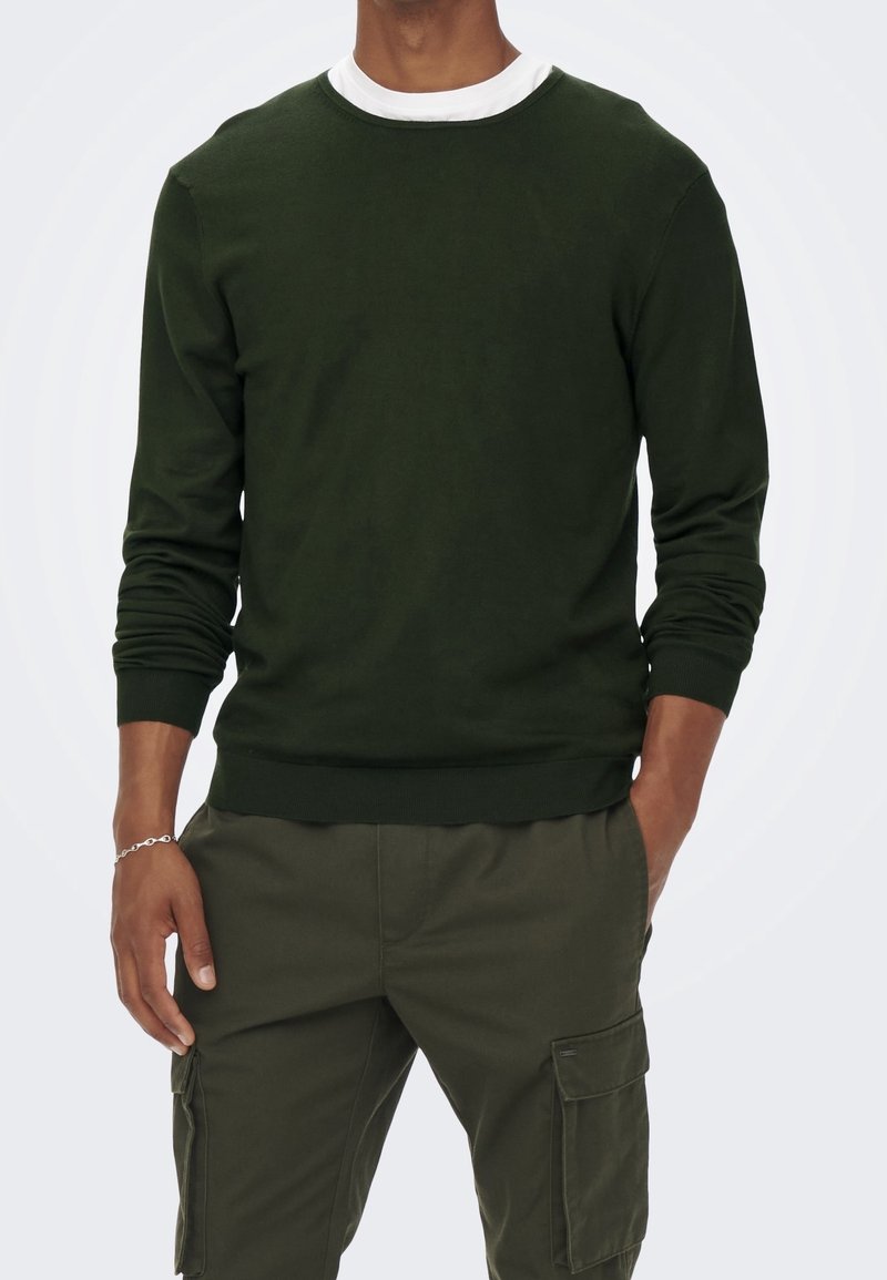 Pull vert foncé avec un col rond blanc, poignets et ourlet côtelés. Porté avec un pantalon cargo assorti, doté de poches latérales.