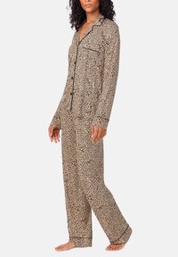 Beżowy komplet piżamowy w panterkę z kontrastującym czarnym obszyciem. Posiada długie rękawy, zapinany na guziki top, kieszeń oraz spodnie o luźnym kroju.