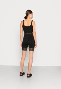 Sort ribbet crop top med brede stropper, parret med sorte biker shorts med blonder trimmet i kanten, båret med sorte sandal.