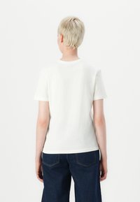 White cotton t-shirt with short sleeves and a round neckline, viewed from the back. Paired with dark blue, wide-leg jeans.