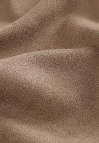 Tissu brun doux et texturé avec une surface légèrement pelucheuse, présentant des variations subtiles de nuances et une apparence lisse et fluide.