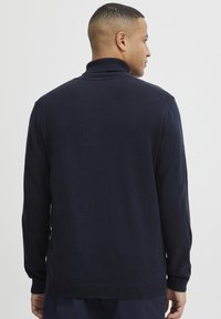 Navy blauwe gebreide trui met een hoge kraag, geribbelde manchetten en zoom. Soepele textuur, minimalistisch design, geschikt voor casual gebruik.