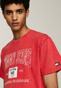 Camiseta de algodón roja con el texto "TOMMY JEANS", cuello redondo, mangas cortas y una etiqueta con el logo en la manga derecha. Corte casual.