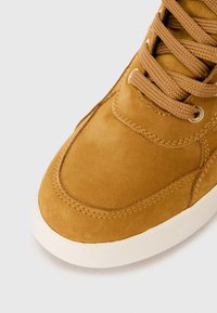 Brune semskede joggesko med en glatt tekstur, rund snøring, hvit gummisåle og kontrasterende sømdetaljer.