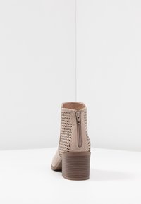 Beige nilon mətbəx ayaqqabısı, kəsilmiş üçbucaqlı naxış, arxa fermuar və 5 sm yığılım dabanı ilə. Yumşaq material və hamar tekstura.
