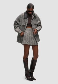 Grå houndstooth oversized jakke over en brun crop top og matchende nederdel. Brune højhælede støvler til knæene. Accessories inkluderer solbriller.