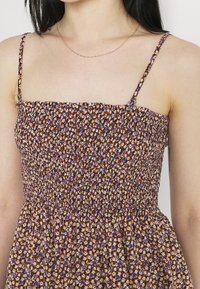 Šaty s květinovým vzorem, na kterých jsou fialové a oranžové květy na světlém béžovém pozadí. Mají nařasený korzet a tenké nastavitelné šle.