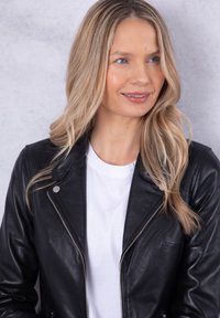 Black leather jacket featuring a zip closure, silver hardware, and a fitted design, worn over a white t-shirt with a crew neckline.