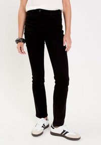 Jeans skinny de cintura alta y color negro con una textura suave, cuentan con cinco bolsillos y cierre de botón. Combinados con zapatillas blancas y grises.