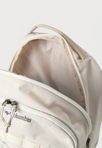 Μπεζ σακίδιο Columbia με φερμουάρ στο άνοιγμα, υφασμάτινη υφή, ραμμένες λεπτομέρειες και πάνω λαβή. Το εσωτερικό είναι λείο και χωρίς επένδυση.