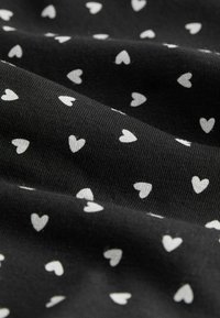 Czarna tkanina z małymi białymi wzorami serc, cechująca się miękką fakturą i lekko rozciągliwą właściwością. Materiał wydaje się być oddychający.