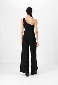Svart ensidig jumpsuit med tettsittende overdel, vide ben og en glatt tekstur. Har bakglidelås og minimal detaljering.