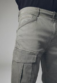 Pantalones cargo grises hechos de un tejido duradero, con bolsillos laterales, acentos de solapa y costuras en contraste, con un corte relajado.