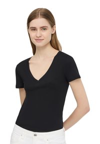 T-shirt nera a V con maniche corte, realizzata in materiale morbido, dalla vestibilità aderente e linee pulite, abbinata a jeans bianchi a vita alta.