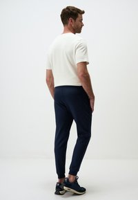 Witte korte mouwen shirt gecombineerd met marineblauwe taps toelopende broek, met een achterzak en aangesloten manchetten, gedragen met donkere sportschoenen.