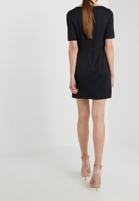 Musta lyhythihainen mekko, jossa on muotoiltu siluetti ja takasauman yksityiskohta, yhdistettynä beigeihin korkokenkiin, joissa on nilkkahihnat.