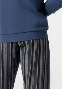 Felpa blu navy con una texture liscia abbinata a pantaloni a righe verticali blu navy e crema, caratterizzati da sottili linee diagonali.