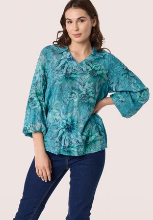Blouse à imprimé floral en teal, avec un col en V, des manches trois-quarts et une coupe ample. Le design comprend des motifs floraux détaillés et des textures.