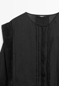 Black sleeveless blouse with round neckline, vertical pleats on front, and lace detailing on the shoulders.
