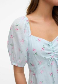 Robe bleu clair avec des manches courtes bouffantes, ornée de motifs floraux roses et d'accents verts. Détail froncé sur le devant central.