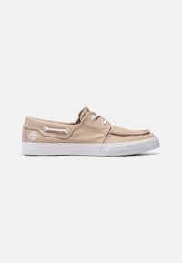 Chaussure bateau en toile marron clair avec lacets blancs, semelle en caoutchouc blanche et logo arbre Timberland sur le côté.