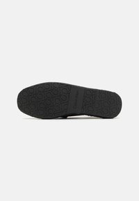 Semelle de chaussure noire en caoutchouc avec un motif texturé, arborant le logo "Calvin Klein". Forme légèrement courbée, sans accents supplémentaires visibles.
