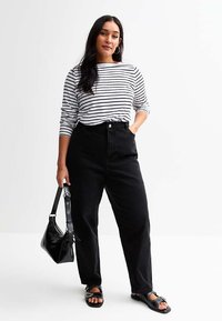 Jeans negros de tiro alto, camisa de manga larga a rayas blancas y negras, sandalias negras y un bolso negro con herrajes plateados.