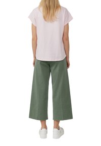 T-shirt rose pâle à manches courtes associée à un pantalon vert à jambes larges et des baskets blanches, mettant en avant une coupe décontractée et une texture de tissu douce.